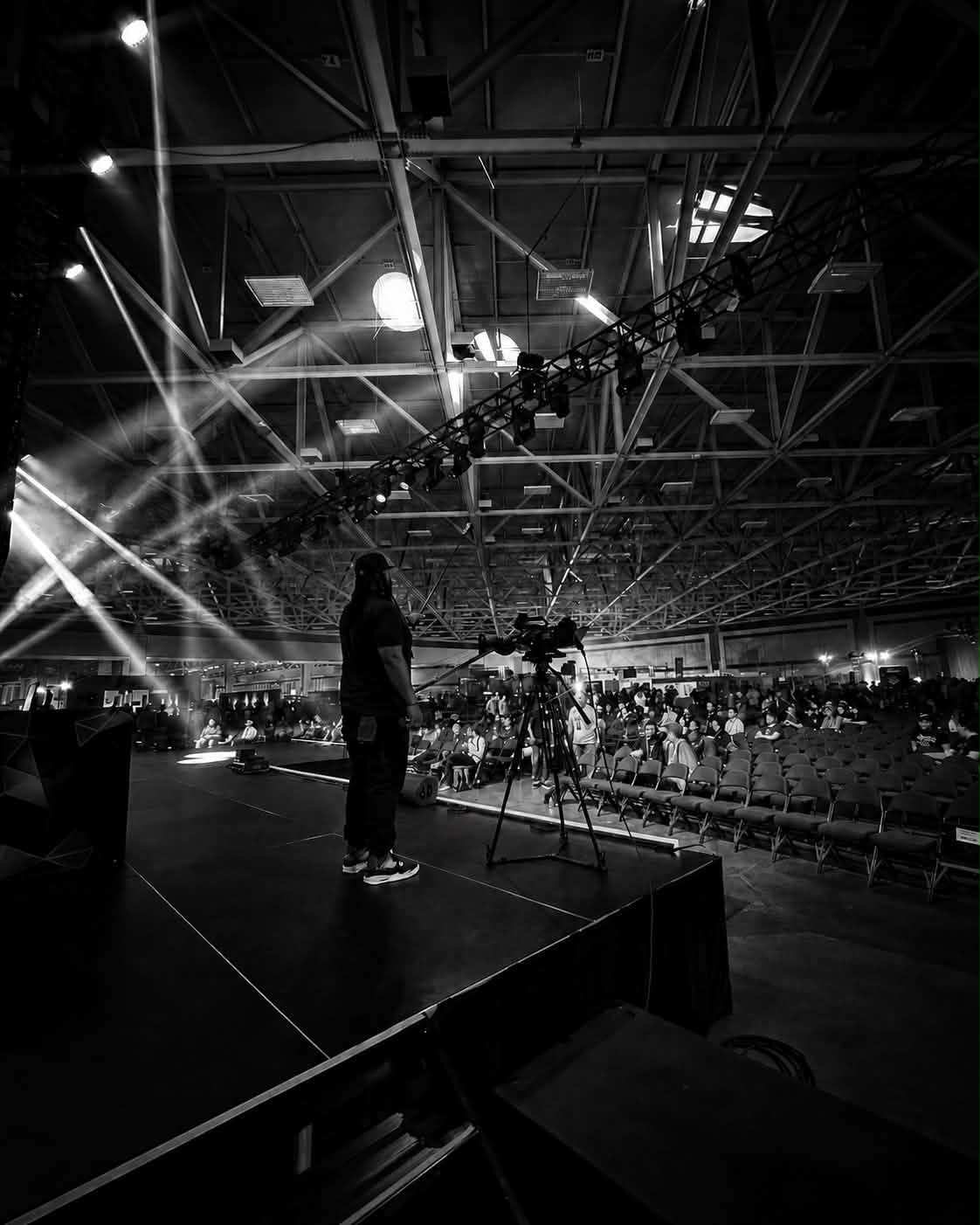 Reggie Washington filming a live event from the stage, a full arena crowd in front of him